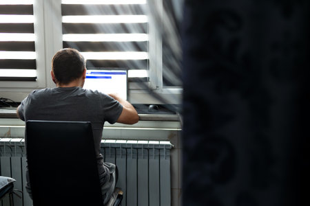Man with laptop working at home, near the window. IT specialist, developer, engineer, programmer at remote work.の写真素材