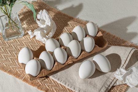 White Easter eggs in eco package and crumpled napkins on a light background with floral sunlight shadows, lifestyle minimalist spring composition with copy spaceの写真素材