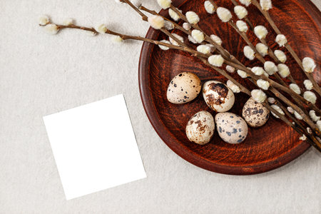 Happy Easter holiday aesthetic template. Blank paper sheet, quail eggs and pussy willow branches on a plate on neutral beige background, stylish rustic composition with copy spaceの写真素材
