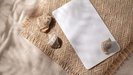 Minimalist aesthetic summer vacation template. Blank paper sheet, sea shells and floral sunlight shadows on a beige textile background.の写真素材