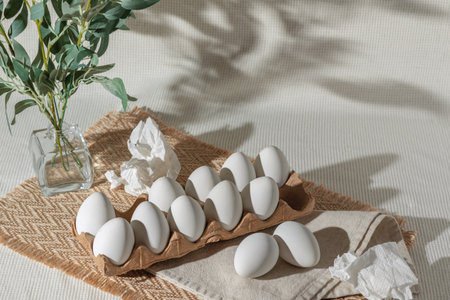White Easter eggs in eco package and crumpled napkins on light background with floral sunlight...