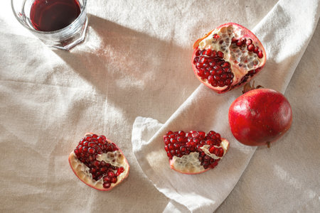 Red juicy pomegranate and wine in a glass on beige linen tablecloth, aesthetic lifestyle background with sunlight shadows, copy spaceの写真素材