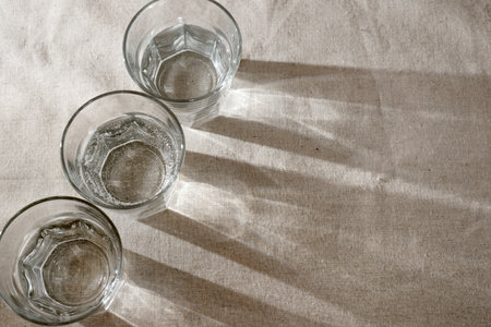 Crystal glasses with water and sparkling sunlight shadows on neutral beige background. Minimalist aesthetic interior modern design conceptの写真素材