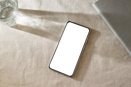 Minimalist classic business mock up, mobile phone with white empty screen on a beige table with sunlight shadowsの写真素材