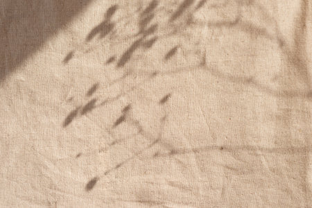 Natural warm neutral beige textile background with floral shadows. Abstract plant silhouette in sunset light on a linen texture curtainの写真素材