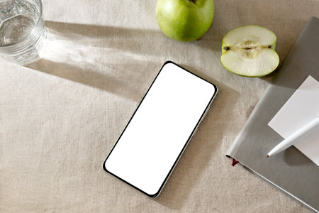 Minimalist elegant lifestyle workspace, mobile phone template with blank white screen, notebook, apples and sunlight shadows on a neutral beige backgroundの写真素材