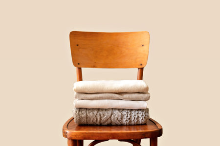 Woman minimalist capsule wardrobe concept, warm pastel colored wool knitted sweaters, pullovers stack on retro wooden chair, on a neutral beige background. Spring, autumn, winter fashion clothes.の写真素材