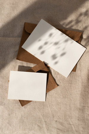 Elegant minimalist business brand template, empty paper card and envelope with floral sunlight shadows on a neutral beige textile background, aesthetic mock up, flat lay with copy spaceの写真素材