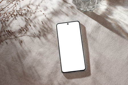 Mobile phone with blank screen mock up on a neutral beige linen background with aesthetic floral sunlight shadows, minimalist business brand, social media blog template, copy spaceの写真素材