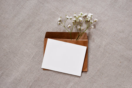 Blank paper card, crafted envelope and flowers on a neutral beige background, minimalist elegant wedding or holiday event invitation, greeting card design template with copy spaceの写真素材
