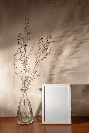 Blank frame mock up, dry meadow grass in glass vase, minimalist interior decoration with aesthetic sunlight shadows on a wall, copy spaceの写真素材