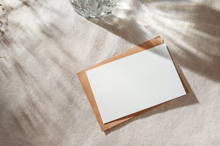 Empty paper card with mock up copy space on a beige table surface with aestethic sunlight shadows, invitation or greeting card, branding templateの写真素材