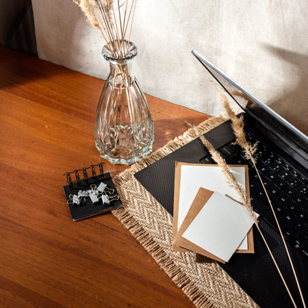 Blank paper cards, laptop, cup of coffee, decorative grass on a brown wooden table, minimalist aesthetic home office workspaceの写真素材