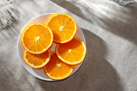 Sliced ripe oranges on plate on a table with aesthetic sunlight shadows, healthy eating, vegan, vitamin source conceptの写真素材