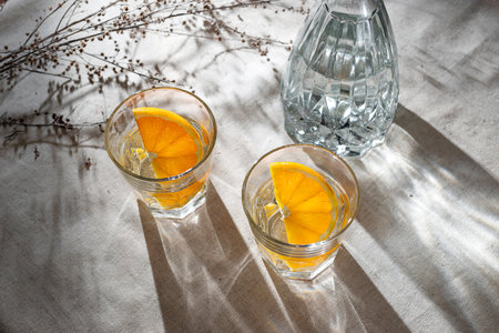 Glasses with orange infused water and bottle on a beige table with aesthetic sunlight shadows, lifestyle healthy drink, vegan conceptの写真素材