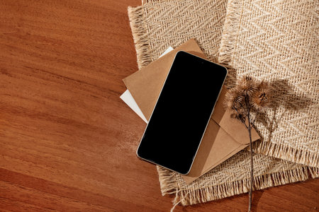 Mobile phone screen mockup, minimalist workspace with smartphone, crafted envelope and flowers dried on a brown table background, copy spaceの写真素材