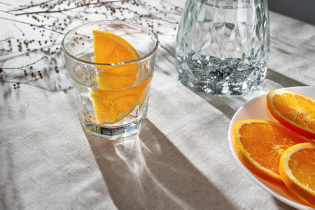 Orange infused water in glass, bottle, sliced oranges on a beige table with aesthetic sunlight shadows, lifestyle healthy drink, vegan conceptの写真素材