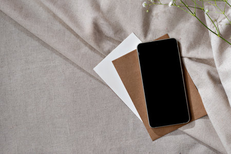 Mobile phone with empty black screen and papers on a neutral beige pleated fabric background, minimalist business branding template with copy space, small business home workspaceの写真素材