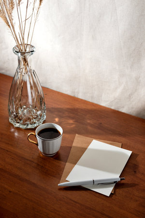 Aesthetic summer interior still life with cup of coffee, paper cards and dry grass in glass vase on a wooden table, floral sunlight shadows, morning business conceptの写真素材