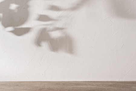Elegant business branding advertisement template with aesthetic foliage sunlight shadows on a neutral beige wall background and wooden floor, empty room interior design layout, mockup with copy spaceの写真素材
