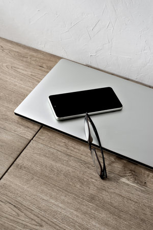 Minimalist business brand concept, laptop, mobile phone and glasses on a beige wooden table, aesthetic home office workspace, copy spaceの写真素材