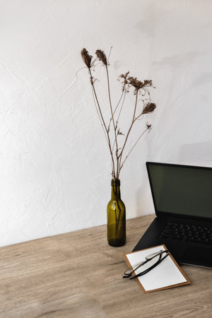 Minimalist business brand composition with copy space, laptop, blank paper card, glasses on a wooden table, home office workspaceの写真素材