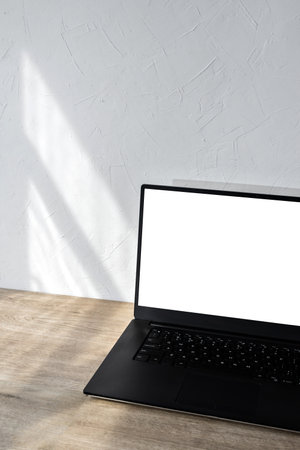 laptop with blank screen mockup on a beige wooden table, aesthetic sunlight shadows on white wall, minimalist business branding template, background with copy spaceの写真素材