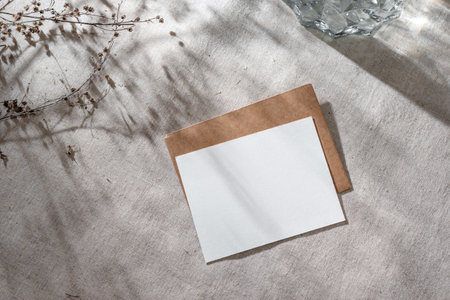 Blank paper card with mock up copy space and envelope on a beige linen background with aesthetic sunlight shadows, invitation or greeting card templateの写真素材
