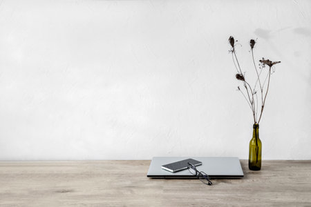Minimalist business brand design template, wooden desk with laptop, mobile phone, vase with flowers, sun light shadows on a white wall background, empty mock up copy spaceの写真素材
