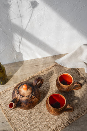 Authentic tea ceremony still life, handcraft clay pottery teapot, muns with tea on a wooden table, aesthetic sunlight shadows on white wall background, sustainable living, wabi sabi conceptの写真素材