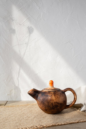 Minimalist handmade ceramic teapot on wooden table, aesthetic sunlight shadows on a white wall background, traditional pottery art concept, copy spaceの写真素材