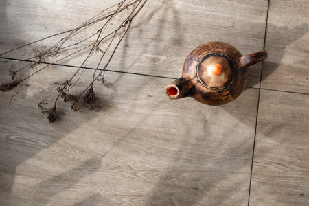Aesthetic tea ceremony concept, crafted clay ceramic pottery teapot and dry flowers on wooden table with aesthetic sunlight shadows, sustainable earthenware background, copy spaceの写真素材