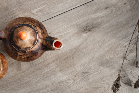 Minimalist wooden table background with a handcraft clay teapot and dried flowers, flat lay, copy spaceの写真素材
