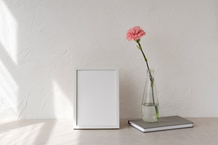 Empty picture frame with mockup copy space, flower in vase on a beige table, empty white wall background with geometric sun light shadow, minimalist aesthetic interior templateの写真素材