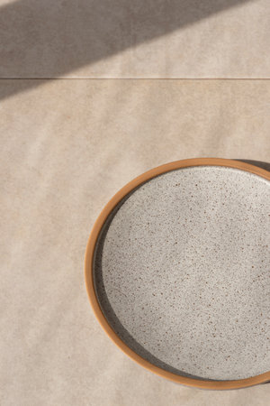 Minimalist background for restaurant or cafe business brand advertisement, neutral gray ceramic empty plate on beige stone table with sunlight shadowの写真素材