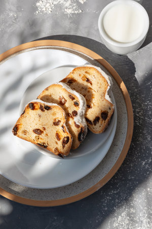 Sliced sweet fruit cake, traditional Christmas stollen on a plate, milk cup on gray background with aesthetic sunlight shadows, lifestyle sweet morning breakfast conceptの写真素材