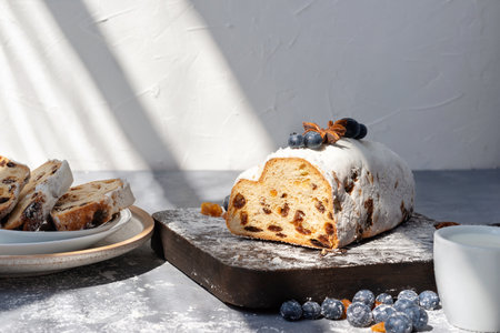 Authentic lifestyle Christstollen sliced on pieces, on a wooden board, with natural sunlight shadows, traditional Christmas stollen decorated with blueberry, raisins, sugar powderの写真素材