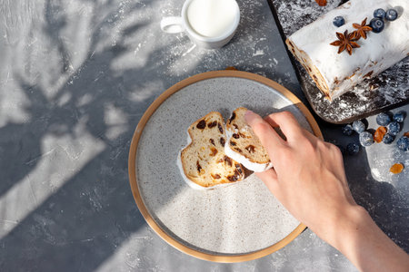 Hand holding piece of stollen, traditional Christstollen sliced on a plate, lifestyle still life with aesthetic sunlight shadows, homemade Christmas sweet cake, tasty morning breakfastの写真素材