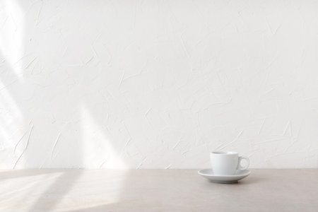Minimalist nordic style good morning concept, cup with drink on a beige table and empty white wall with aesthetic natural sunlight shadows and copy spaceの写真素材