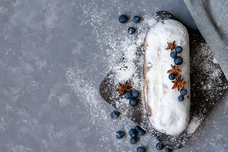 Aesthetic holiday Christmas dessert, stollen decorated with blueberry, raisins, sugar powder on a wooden board on gray background, authentic homemade German bakery, copy spaceの写真素材