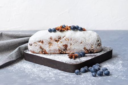 Traditional Christmas German holiday fruit bread, stollen with raisins, decorated with sugar icing and blueberries, on a gray background, white wall copy spaceの写真素材