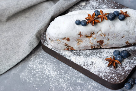 Christstollen, traditional Dresden Christmas stollen, festive fruit bread decorated with blueberry, anise, sugar powder, raisins, on wooden board on a gray backgroundの写真素材