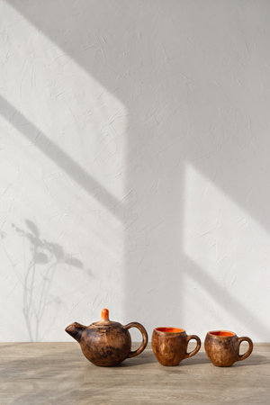 Minimalist kitchen interior design tea set, crafted clay pottery teapot and mugs on wooden table, aesthetic sunlight shadows on a wall, copy spaceの写真素材