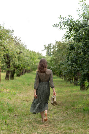 Sustainability, environmental and ecology nature care concept, woman in dress walking barefoot on green grass outdoor in park, holding heeled shoes in her handの写真素材