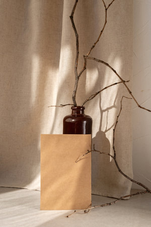 Blank brown crafted card mock up, vase with dried tree branches on table with aesthetic sunlight shadow on beige linen curtain background, elegant neutral business brand, wedding invitation templateの写真素材