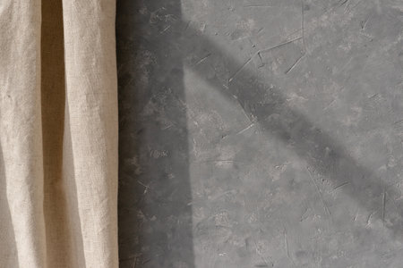 Empty gray concrete wall texture and beige linen curtain, minimalist neutral interior design background, home room backdrop with a sun light shadowの写真素材