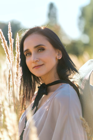 Sincere attractive middle age woman in summer meadow grass, with spikelets near face, walking outdoor in a nature, enjoying and smiling, calm and serenity conceptの写真素材