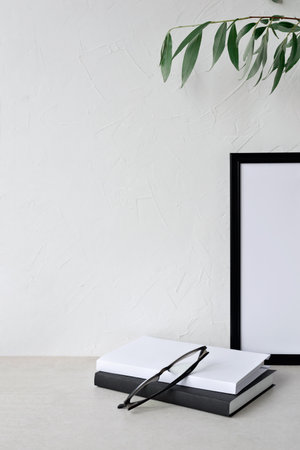 Minimalist business branding template, neutral beige empty wall mockup background, picture frame, books and glasses on a tabletop, minimalist modern home interior workspace, lagom conceptの写真素材