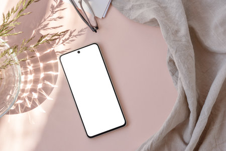 Blank smartphone screen mock up, linen textile, glass vase with meadow grass stems on a neutral light pastel pink background with sunlight shadow. Aesthetic feminine business brand identity templateの写真素材