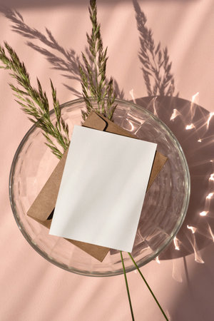 Empty paper card mockup, envelope, meadow grass, glass vase on a neutral light peach, beige background with aesthetic sunlight shadow, boho wedding invitation templateの写真素材